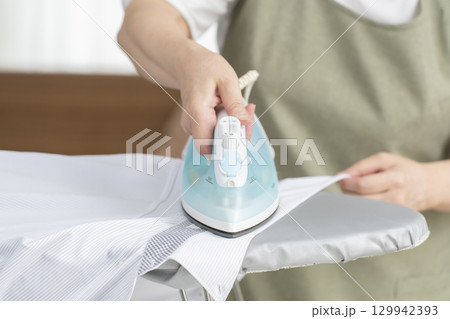 リビングでワイシャツにアイロンを描けるシニア女性(顔無) リビングでワイシャツにアイロンを描けるシニア女性(顔無) 129942393