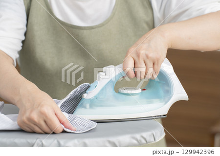 リビングでワイシャツにアイロンを描けるシニア女性（顔無） 129942396