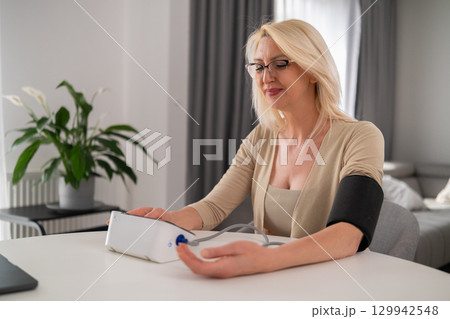 londe woman in beige clothes measuring blood pressure on modern home device, appearing focused and attentive in modern living room londe woman in beige clothes measuring blood pressure on modern home device, appearing focused and attentive in modern living room 129942548