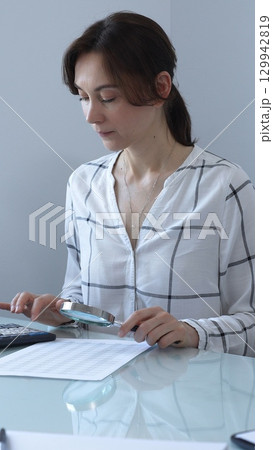 Accountant carefully reviewing financial documents, magnifying details, calculating performance metrics at professional workspace. Audit and taxes in business 129942819