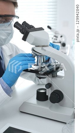 Man scientist wearing protective googles and blue gloves, is using microscope analyzing samples in modern laboratory doing scientific research. Medicine and science concept Man scientist wearing protective googles and blue gloves, is using microscope analyzing samples in modern laboratory doing scientific research. Medicine and science concept 129942840