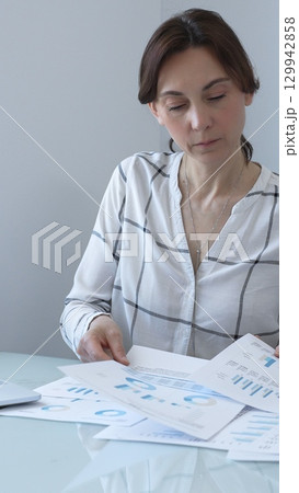 Businesswoman reviewing financial data, analyzing charts and graphs while working on a project at her office desk, demonstrating focus and expertise in business management. Business people concept 129942858