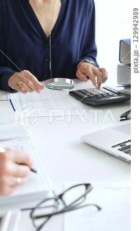 Financial analysts examining documents, using magnifying glass and calculator while studying corporate data at workplace. Audit and taxes in business 129942989