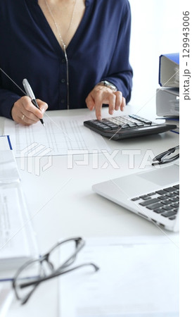 Female financial analysts examining documents, using magnifying glass and calculator while studying corporate data at workplace. Audit and taxes Female financial analysts examining documents, using magnifying glass and calculator while studying corporate data at workplace. Audit and taxes 129943006