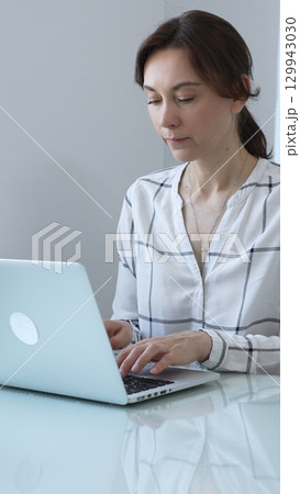 Professional businesswoman working on laptop, sitting at glass desk in bright contemporary workspace, embodying corporate success and concentration. Business people concept. Professional businesswoman working on laptop, sitting at glass desk in bright contemporary workspace, embodying corporate success and concentration. Business people concept. 129943030