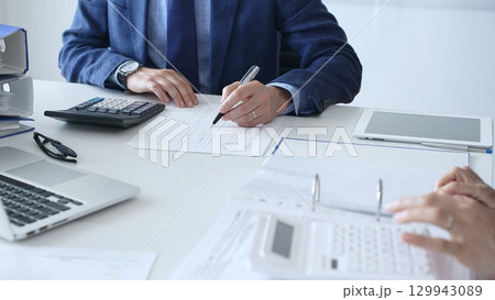 Close up of female accountant hands using calculator while collaborating with male colleague in office, calculating taxes and analyzing financial data. Audit and taxes in business 129943089