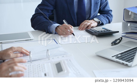 Close up of female accountant hands using calculator while collaborating with male colleague in office, calculating taxes and analyzing financial data. Audit and taxes in business 129943094