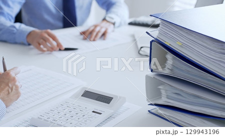 Two accountants collaborating in a bright office, analyzing financial documents and using a calculator with a laptop displaying charts. Audit and taxes in business 129943196