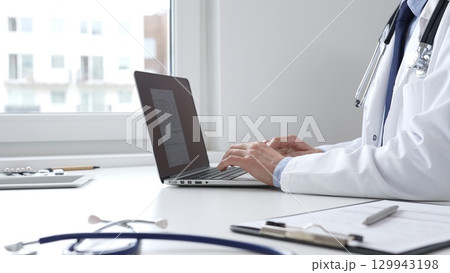 Medical professional typing on laptop, updating electronic patient records with focused concentration, representing digital transformation in healthcare workplace 129943198