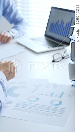 Two professional auditors reviewing financial documents, working collaboratively at white desk with blue folder stack, highlighting teamwork. Audit and taxes in business 129943215