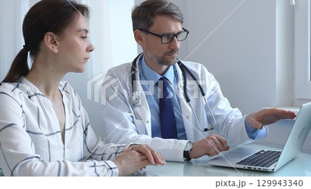 Male doctor showing medical test results on a laptop to a female patient, discussing diagnosis and treatment options in a bright medical office. Medicine and health care Male doctor showing medical test results on a laptop to a female patient, discussing diagnosis and treatment options in a bright medical office. Medicine and health care 129943340