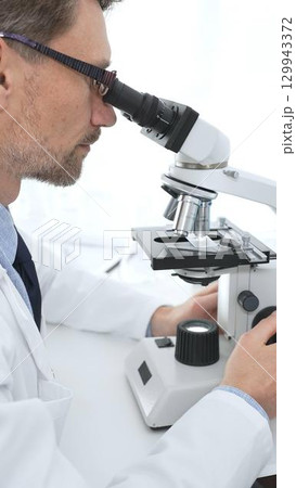 Medical scientist wearing glasses using microscope analyzing samples in modern laboratory doing scientific research. Medicine, health care and science concept Medical scientist wearing glasses using microscope analyzing samples in modern laboratory doing scientific research. Medicine, health care and science concept 129943372