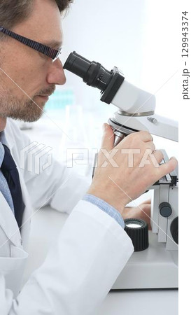 Medical scientist wearing glasses using microscope analyzing samples in modern laboratory doing scientific research. Medicine, health care and science concept 129943374