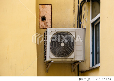 dirty air conditioner unit is mounted on a yellow wall. ventilation and cooling of the home. dirty air conditioner unit is mounted on a yellow wall. ventilation and cooling of the home. 129946473
