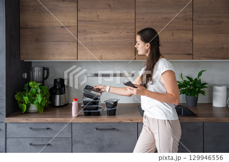 Young woman with healthy diet plan for weight loss, delivery of daily ready meal menu. Woman using meal tracker app on phone. Balanced portion with dish. Pre-cooking. 129946556
