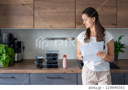 Young woman with healthy diet plan for weight loss, delivery of daily ready meal menu. Food ordered with mobile phone app. Balanced portion with dish. Pre-cooking. 129946561