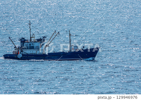 Fishing boat in blue sea and clear sky with birds flying overhead. 129946976