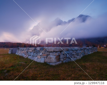 Mountain landscape at dawn. Sunbeams in a valley. Foggy weather in the mountain valley at dawn. 129947118
