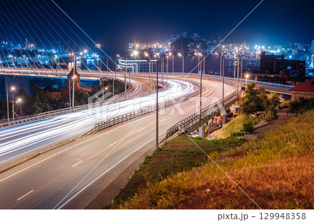 Glowing light trails streaming across zolotoy bridge during nighttime, revealing vibrant cityscape of vladivostok, russia Glowing light trails streaming across zolotoy bridge during nighttime, revealing vibrant cityscape of vladivostok, russia 129948358