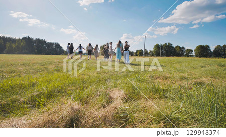 High school students walking hand in hand through a vast field during their summer vacation 129948374