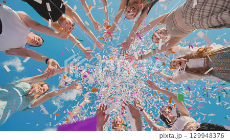 High school graduates joyfully tossing confetti in the air against a backdrop of clear blue sky 129948376