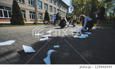 Students gathering loose papers in the schoolyard on the final day of school 129948445