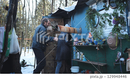 Two homeless people entering their makeshift home built with recycled materials in a winter forest, symbolizing poverty and social exclusion Two homeless people entering their makeshift home built with recycled materials in a winter forest, symbolizing poverty and social exclusion 129948446