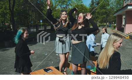 Cheerful students dancing on school desks outside the building, celebrating the end of the school year 129948450