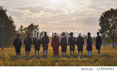 Graduates in academic attire and caps standing in a field at sunset following their graduation Graduates in academic attire and caps standing in a field at sunset following their graduation 129948465