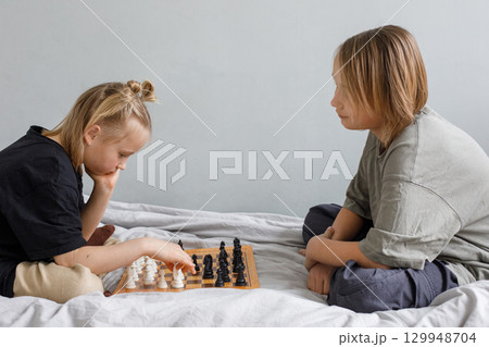 Cheerful boy and girl playing chess board game while thinking of move with knowledge 129948704