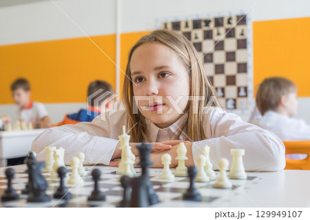 Pretty schoolgirl playing chess game in school classroom. Child girl on chess lesson strategy 129949107