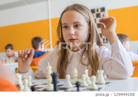 Cheerful child school student on chess lesson indoor. Young girl 10 years old playing chess 129949108