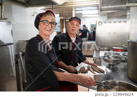 Two chefs in black uniforms working together while serving freshly fried fish in a commercial kitchen. Concept of seafood preparation, teamwork, culinary skills, and hospitality industry. Two chefs in black uniforms working together while serving freshly fried fish in a commercial kitchen. Concept of seafood preparation, teamwork, culinary skills, and hospitality industry. 129949824