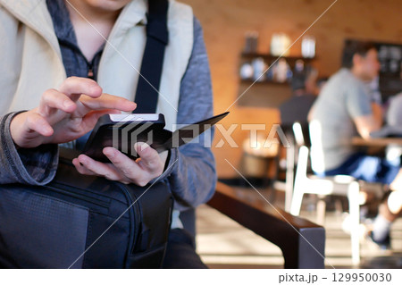 Close-up of a woman browsing drink menu on cell phone inside coffee shop 129950030