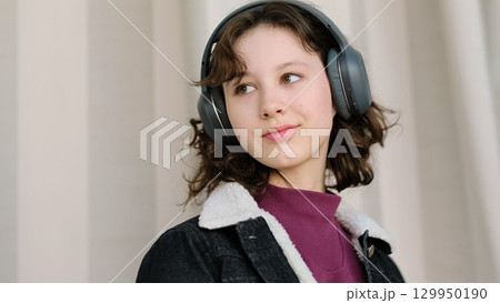 A thoughtful girl wearing headphones appears deeply engaged with her own world. The image symbolizes personal focus, creative thinking, and the emotional connection to sound. 129950190