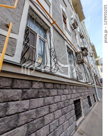 A textured facade of a building featuring iron-barred windows and rugged stone walls. The contrast of industrial elements highlights themes of security and urban resilience. 129950205