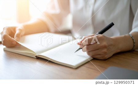 机の上でノートに書いている女性の手 129950371