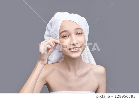 Young caucasian female applying under eye mask in skincare routine with towel 129950593