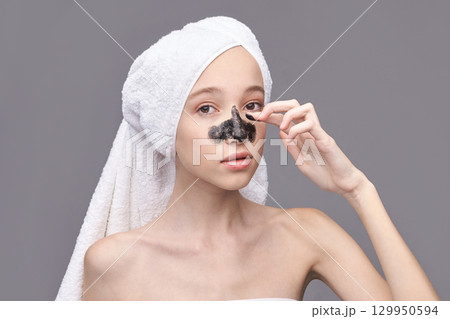 Young caucasian female applying blackhead removal mask with towel wrapped hair Young caucasian female applying blackhead removal mask with towel wrapped hair 129950594