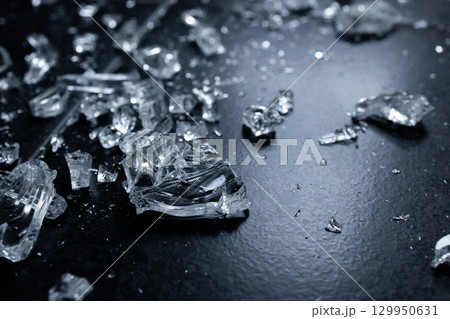 Close up of shattered glass pieces on dark surface showing textures and reflections 129950631