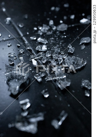 Shattered glass pieces scattered on black surface in low light 129950633