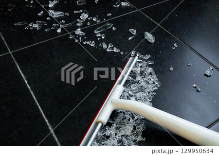 Broom sweeping broken glass shards on black tiled floor for safe clean up Broom sweeping broken glass shards on black tiled floor for safe clean up 129950634