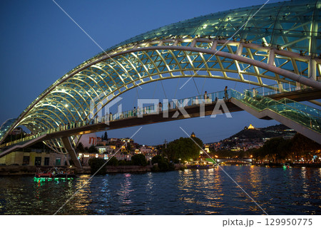 Peace bridge, steel and glass construction pedestrian bridge over Kura Mtkvari river in central Tbilisi, capital of Georgia 129950775