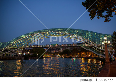 Peace bridge, steel and glass construction pedestrian bridge over Kura Mtkvari river in central Tbilisi, capital of Georgia 129950777