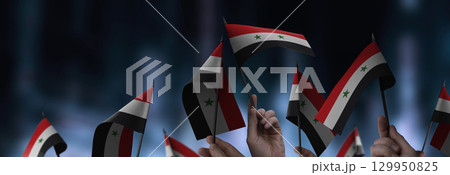 Syria flags in their hands on a blurred urban background 129950825