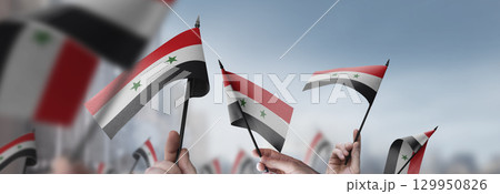 Syria flags in their hands on a blurred urban background 129950826