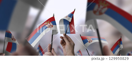 Serbia flags in their hands on a blurred urban background 129950829