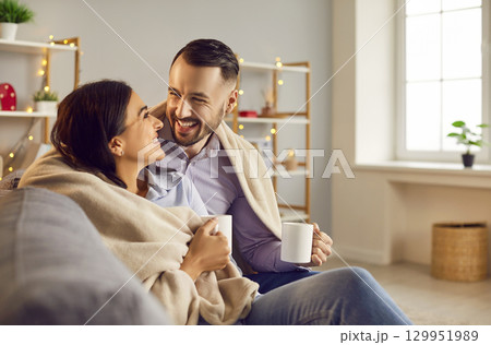 Happy laughing couple in love sitting on sofa at home with a cup of tea and looking at each other Happy laughing couple in love sitting on sofa at home with a cup of tea and looking at each other 129951989