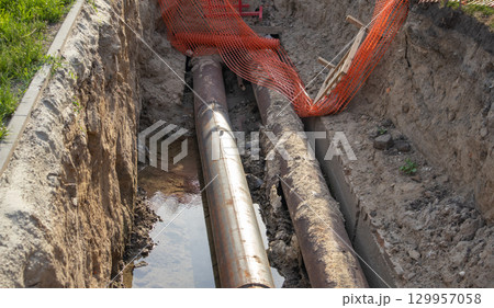 Close-up, repair of a heating main, laying of large-diameter metal pipes in a trench, protective warning signs 129957058