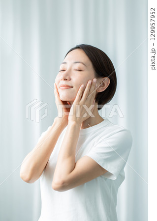 両手で頬に触れて潤いの浸透を実感する透明感のある女性 目をつむる上半身 両手で頬に触れて潤いの浸透を実感する透明感のある女性 目をつむる上半身 129957952